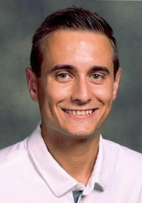 A smiling person wearing a white collared shirt against a dark, mottled grey background.