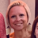 A person with blonde hair smiling while wearing large, light-colored circular earrings.
