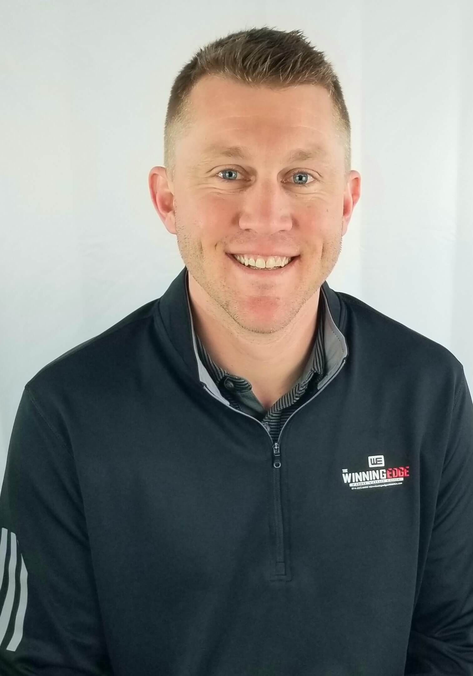 Headshot of a smiling person wearing a dark blue, long-sleeved quarter-zip pullover against a white background.