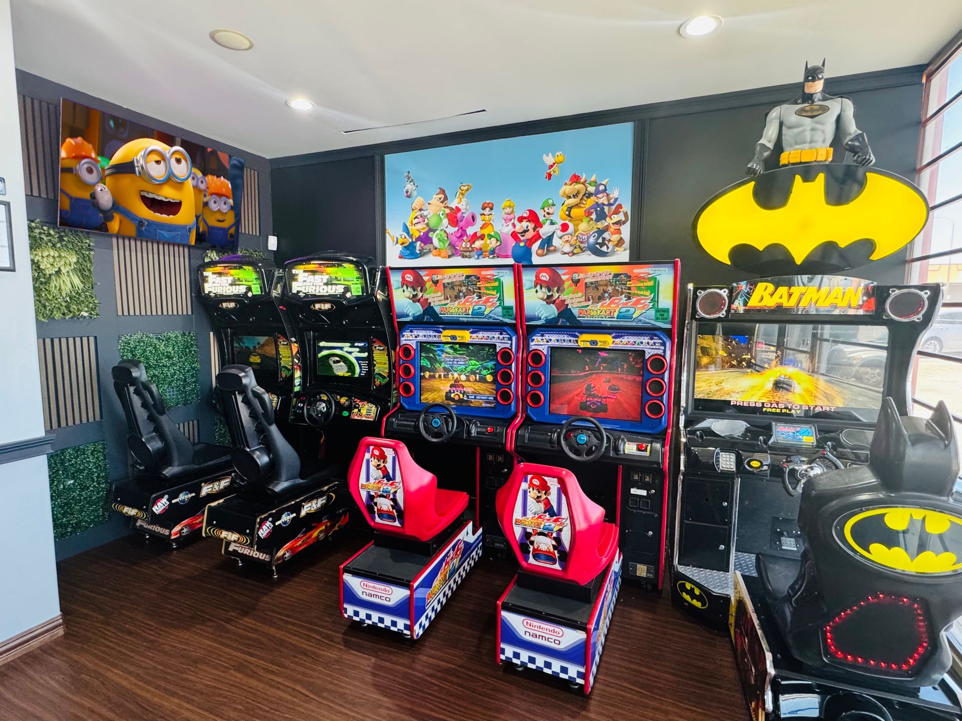 Batcave-themed arcade room with Batman machines, racing cabinets, and pink gaming chairs