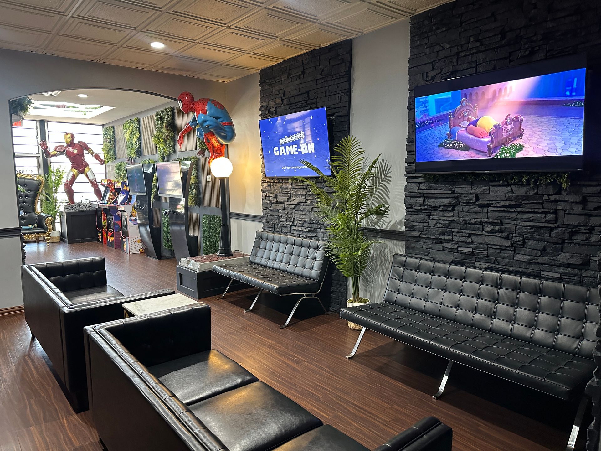 Modern lounge with black tufted benches, wooden tables, wall-mounted TVs, and potted plants.