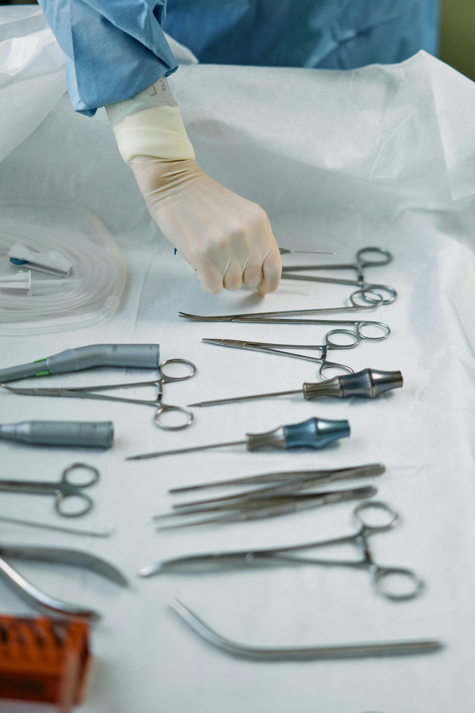 Gloved hand reaching for a surgical instrument on a sterile table with other tools.