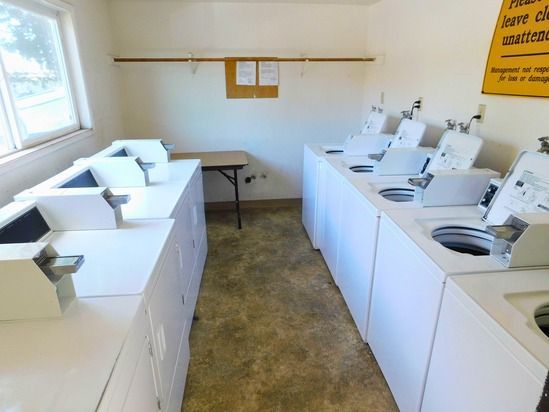 Laundry room with white washers and dryers. A small table is between them. Beige floor and walls.