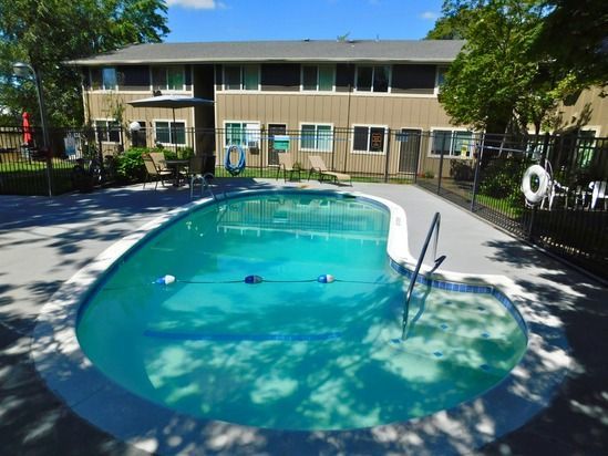 Swimming pool in front of a two-story tan apartment building, surrounded by a black fence.