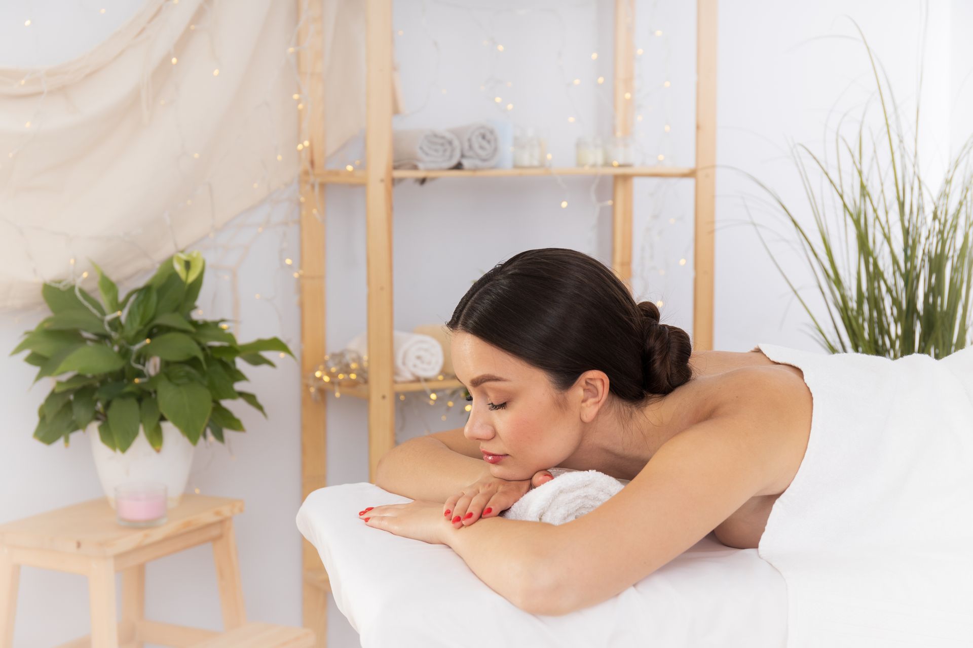 Woman resting her head on folded arms beside a white bed in a bright spa room