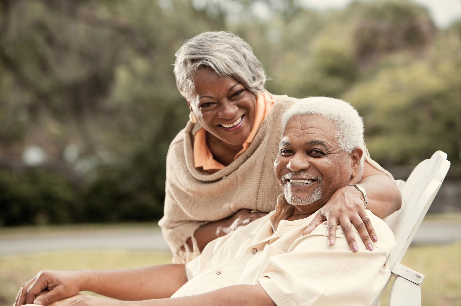 An elderly couple is sitting in a chair and smiling for the camera.