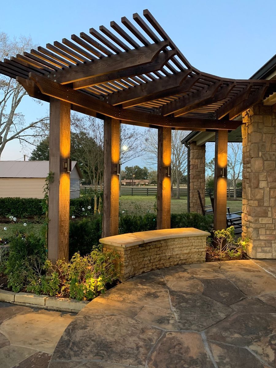 Wooden pergola with built-in stone bench beside a landscaped garden path at dusk