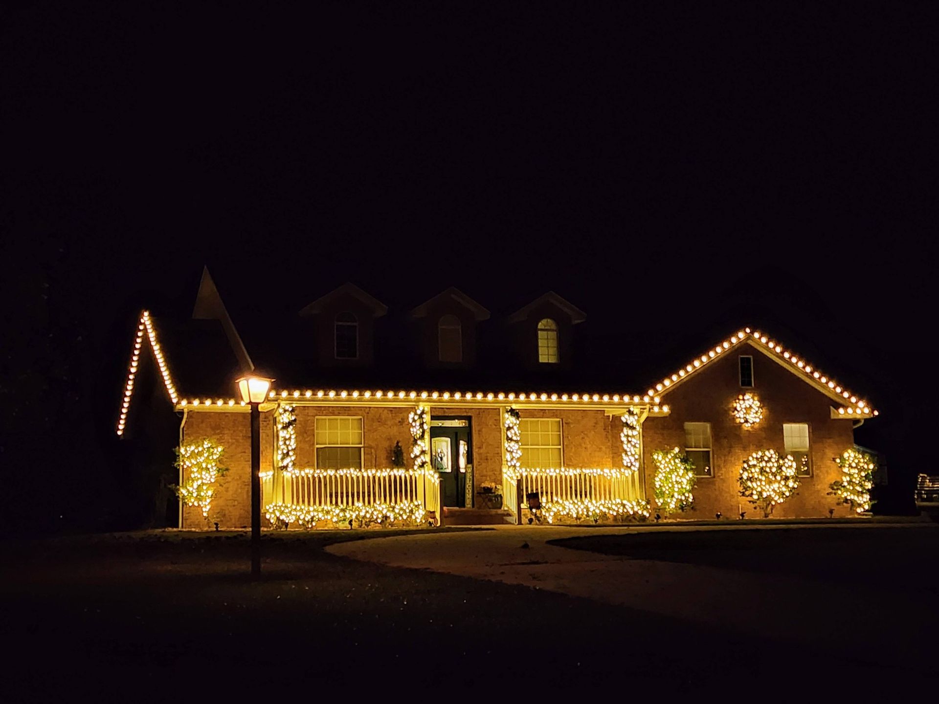 House outlined in warm white holiday lights at night, with a lit wreath on the front and garage.