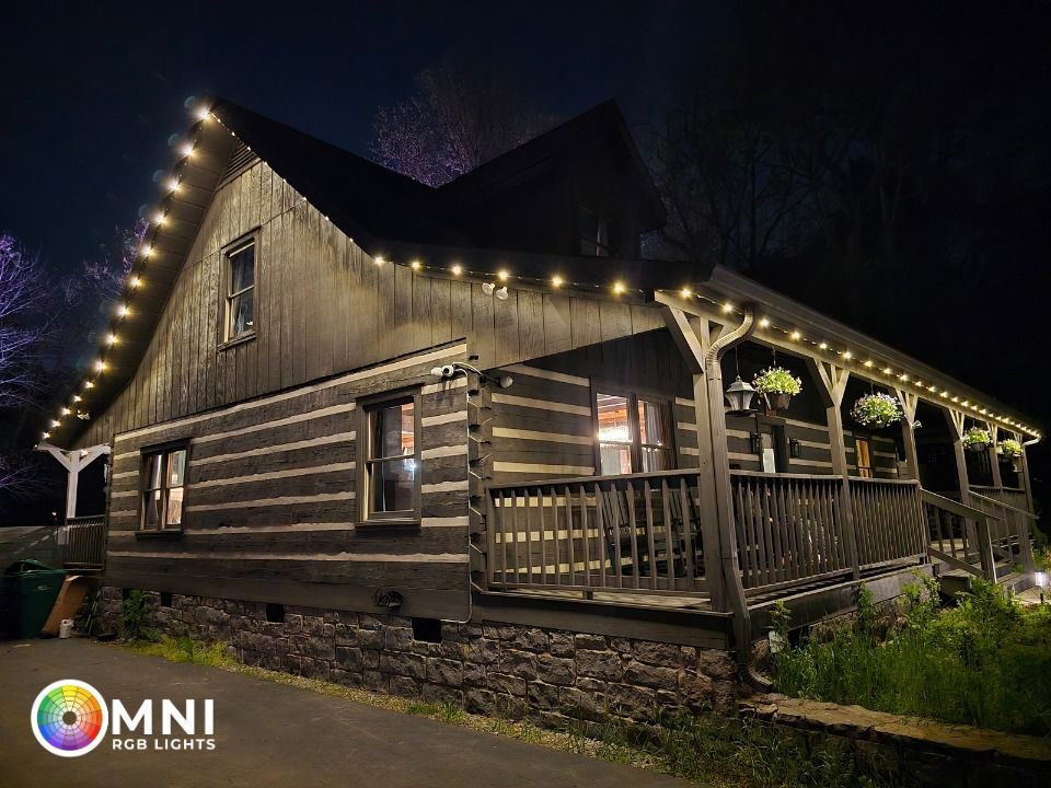 Rustic log cabin at night with warm string lights and a covered porch in a wooded setting