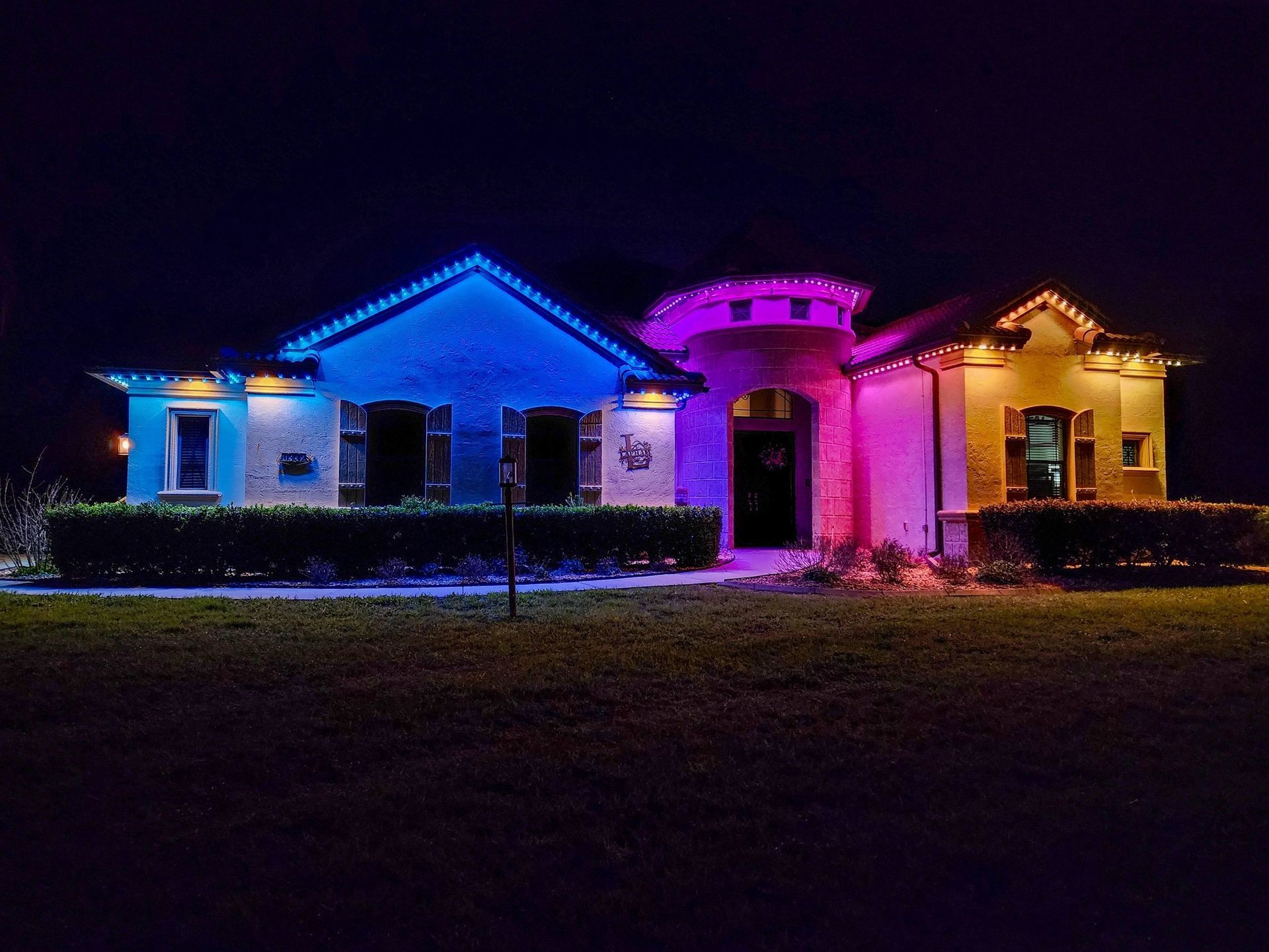 House lit with blue, pink, and purple holiday lights at night