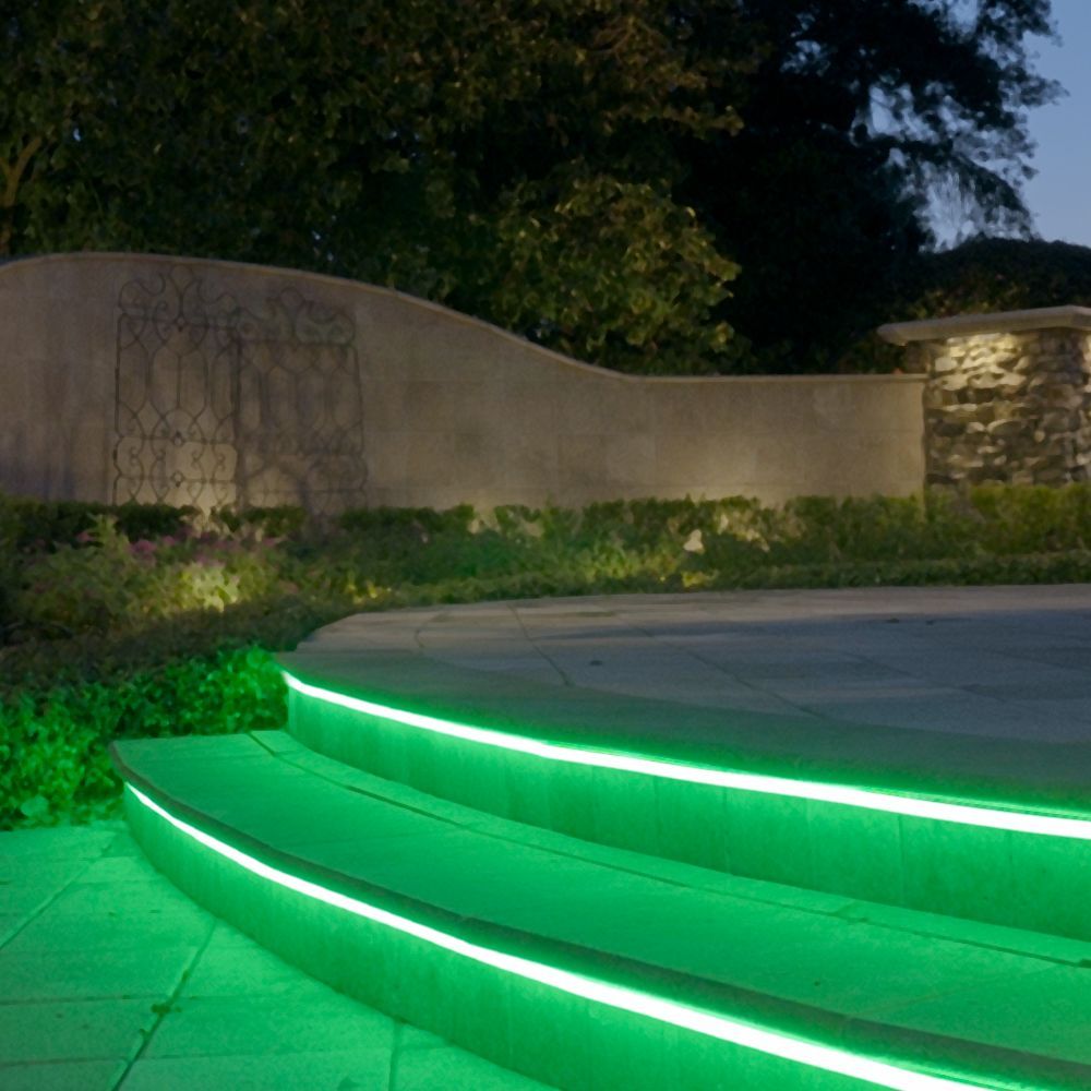 Curved outdoor steps with bright green LED lights at dusk beside a stone wall and shrubs