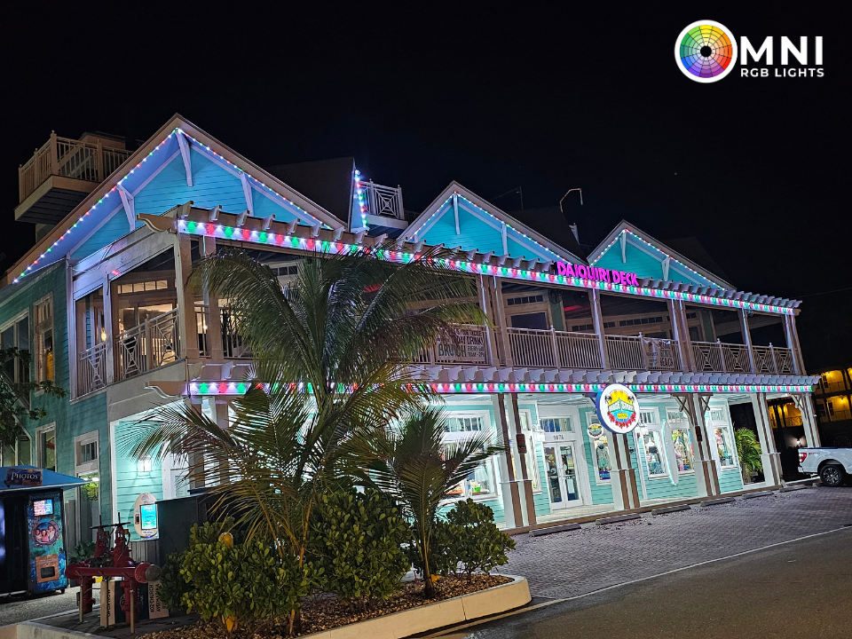 Nighttime view of a lit two-story building with neon trim and palm landscaping, likely a restaurant or hotel