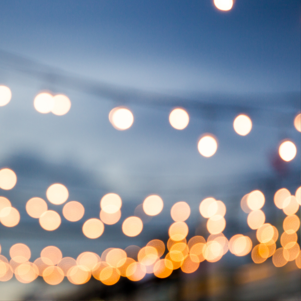 Blurred string lights glowing against a twilight blue sky with warm orange bokeh