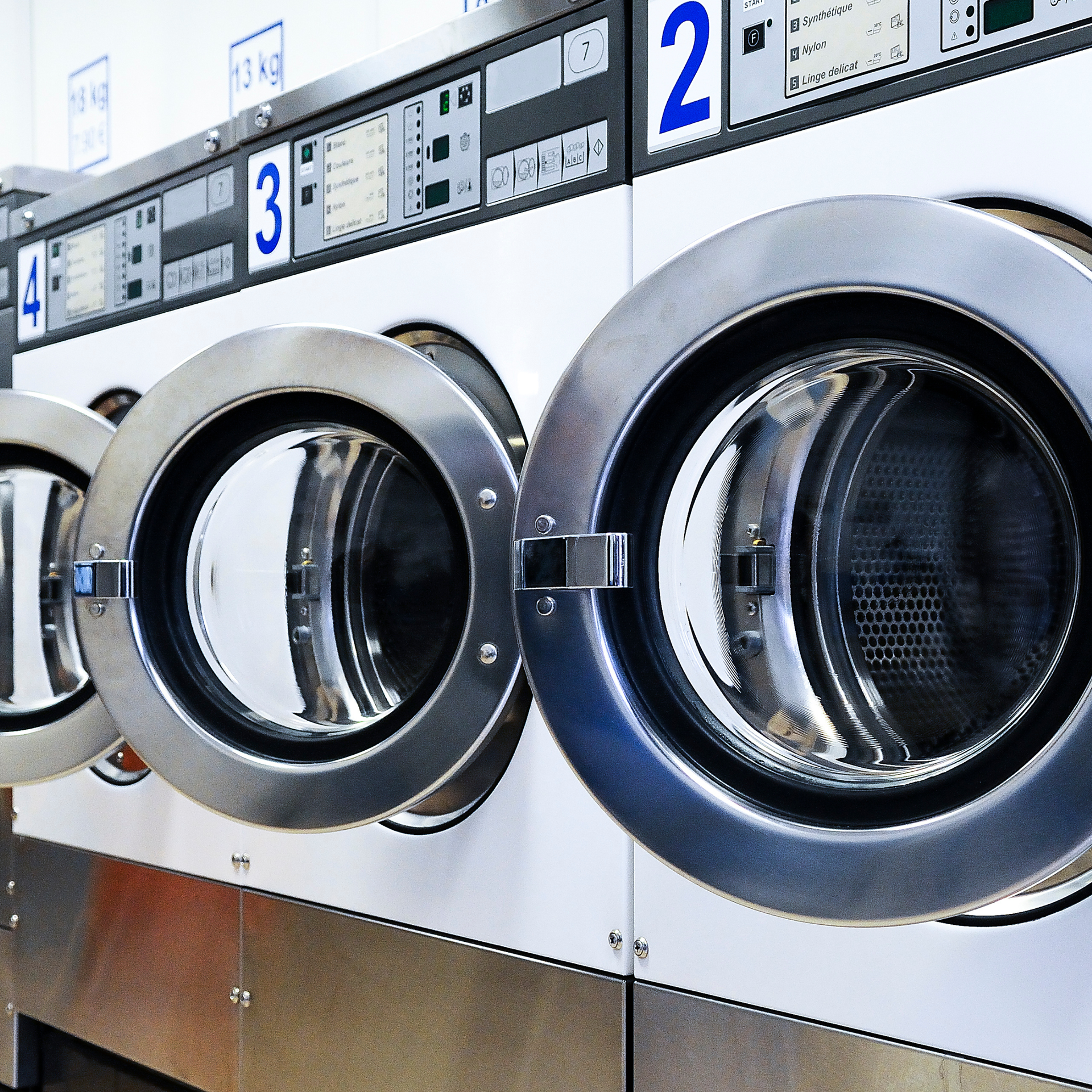 Row of stainless steel front-loading washing machines in a laundromat