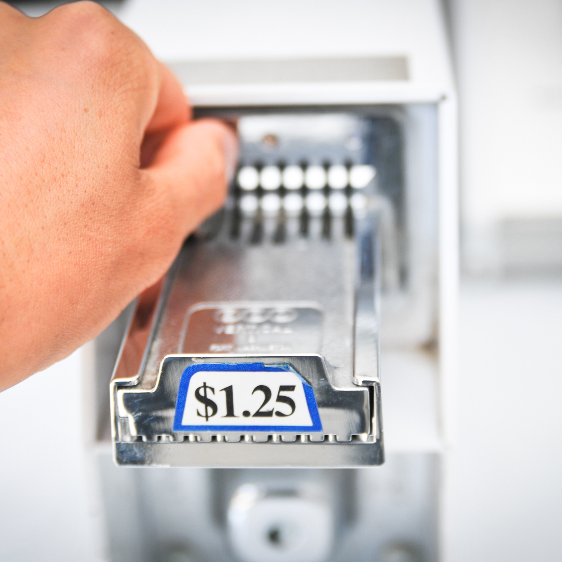 Hand inserting a $1.25 coin into a vending machine slot