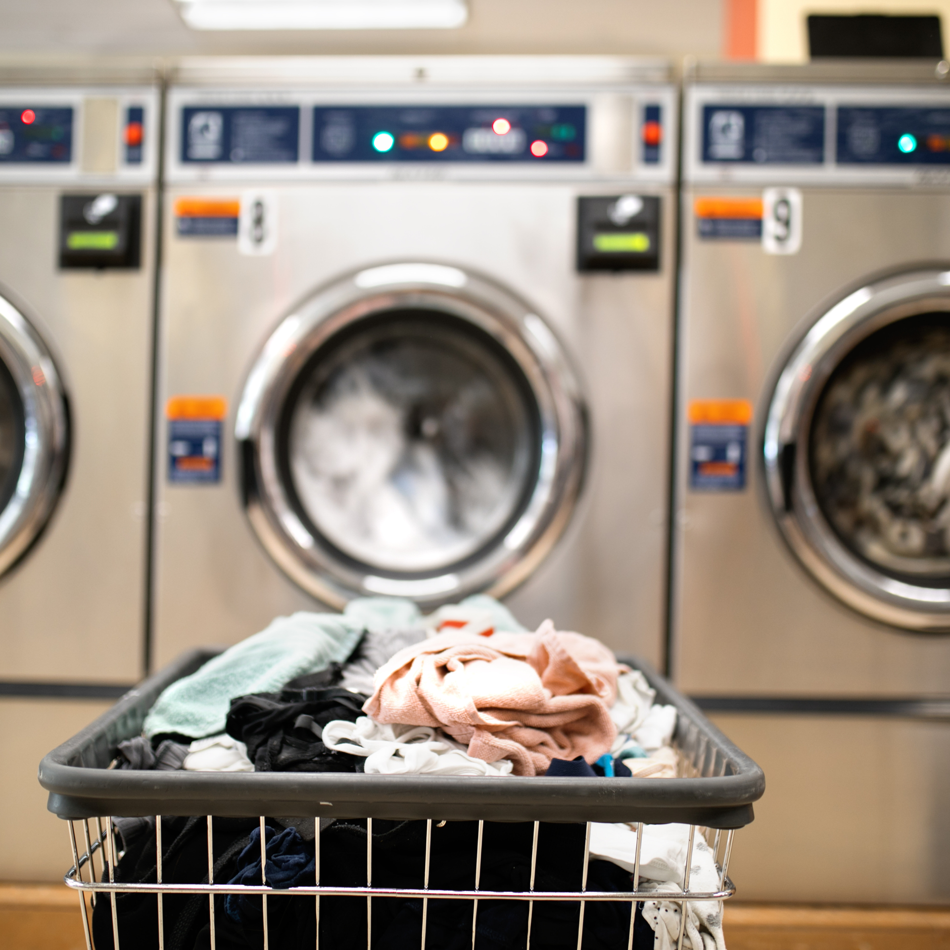 Laundry basket of clothes in front of washing machines in a laundromat.