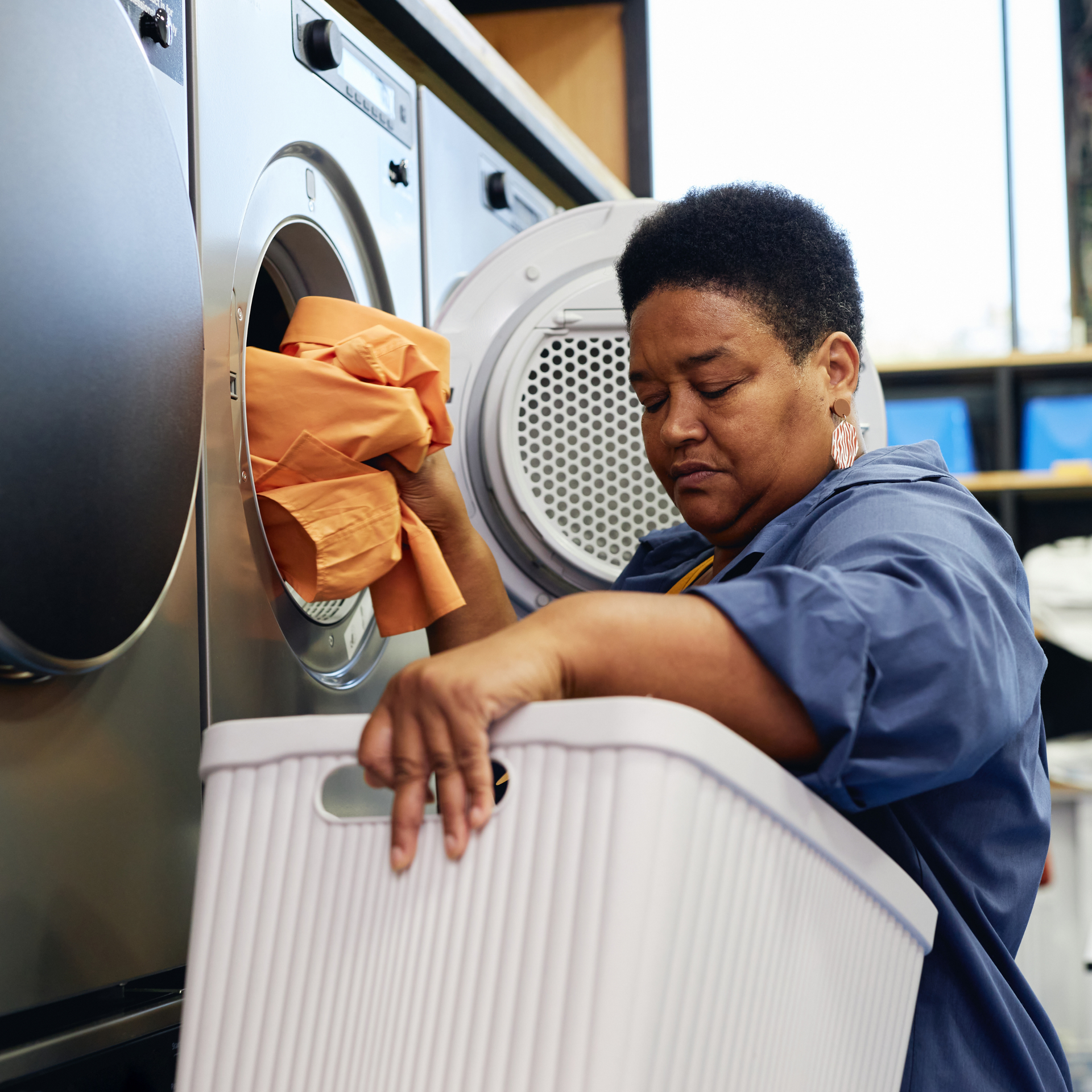 Person loading laundry from a dryer into a white basket in a laundromat