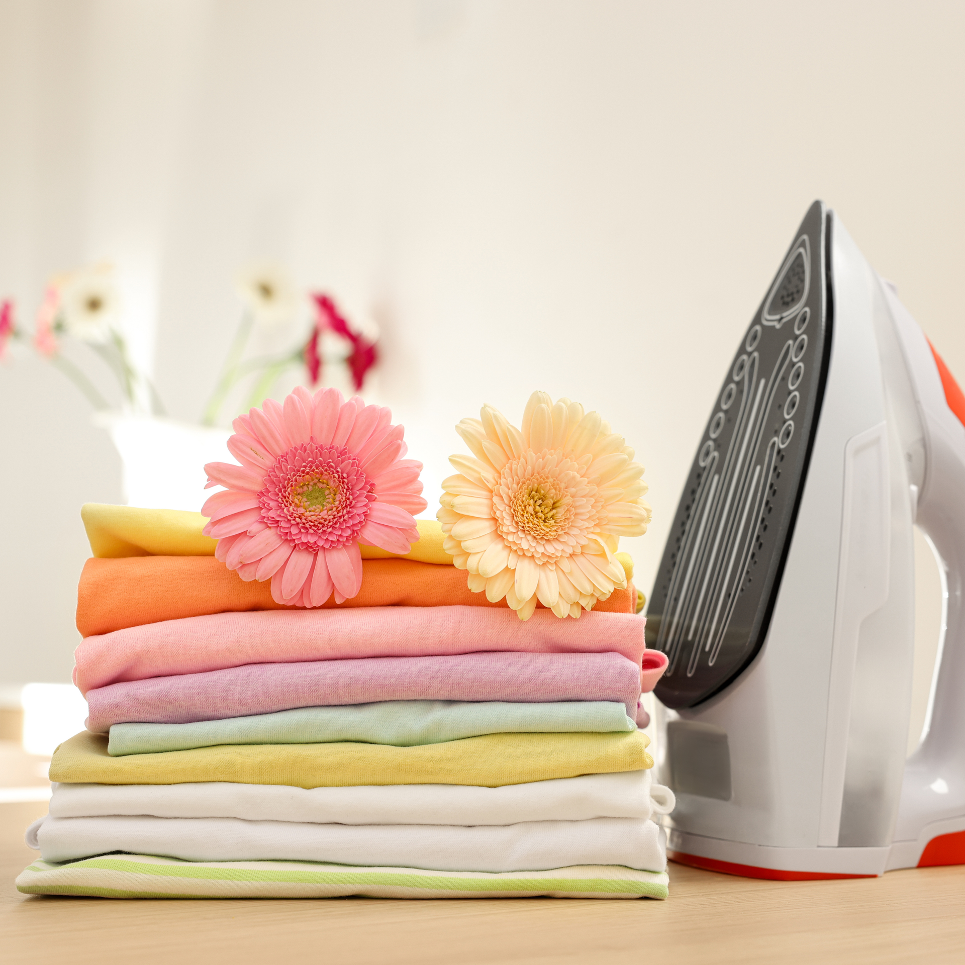 Stack of colorful folded towels with flowers beside an upright iron on a bright surface
