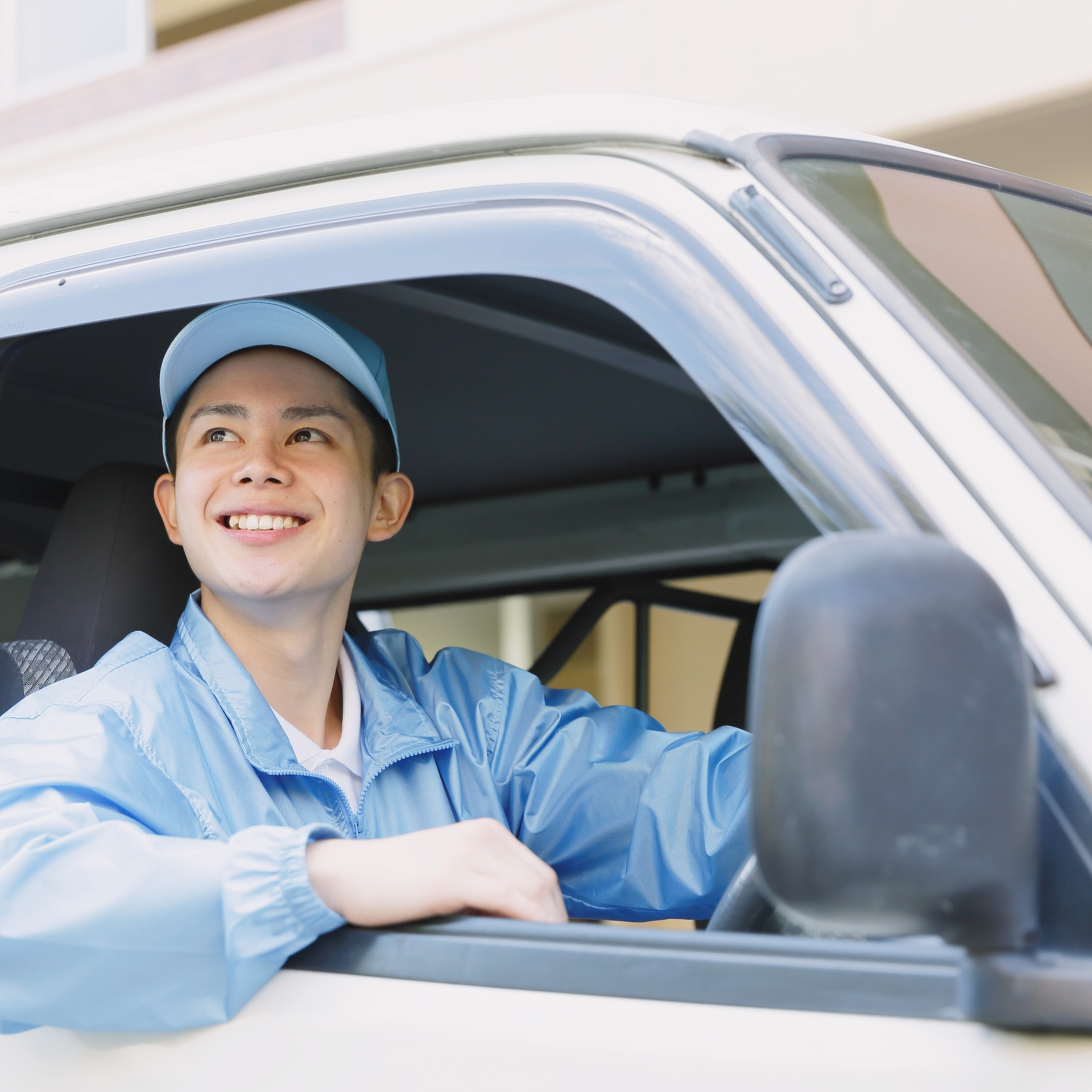 Smiling delivery driver in blue uniform seated in a van, looking out the open window