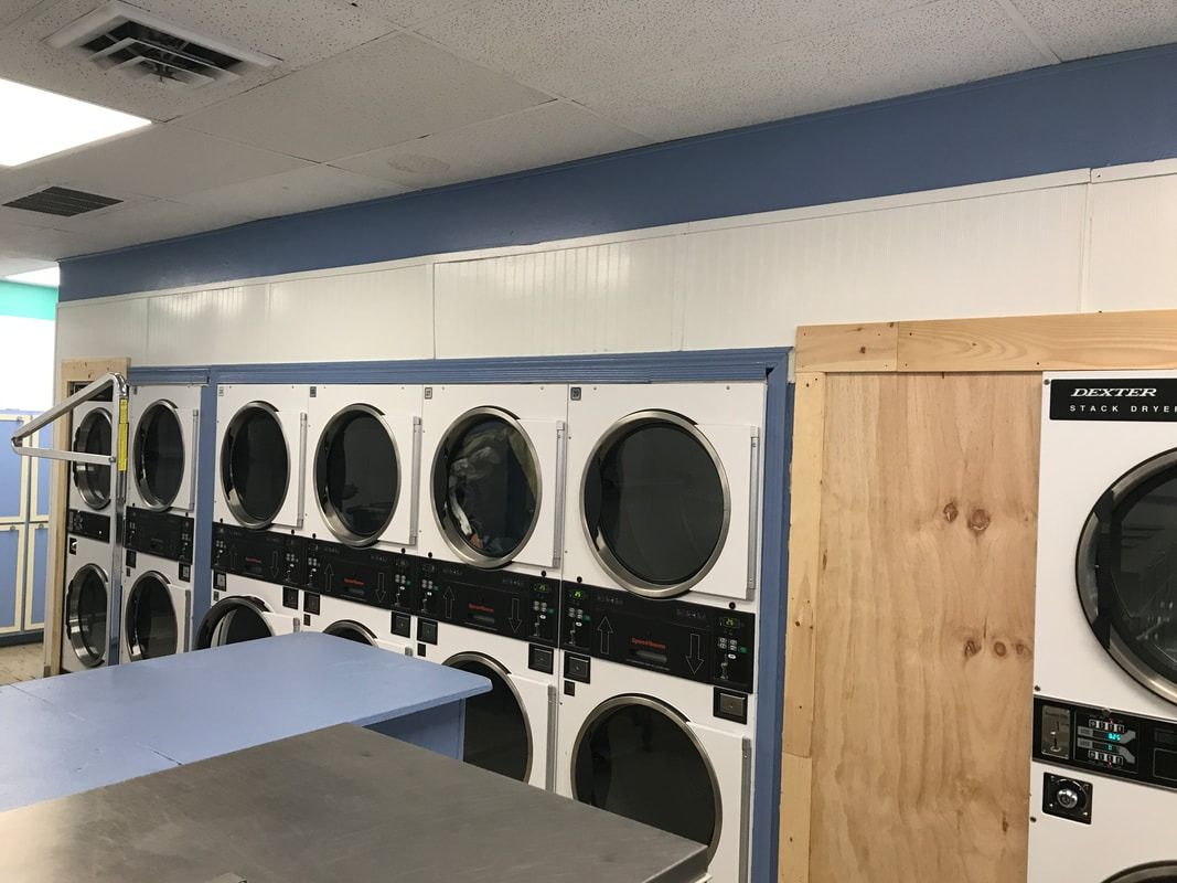 Laundry room with rows of stacked industrial dryers and a blue folding table in the foreground