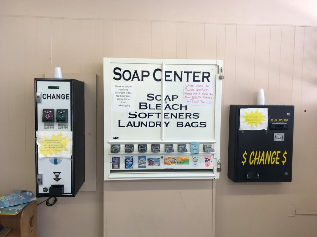 Soap center signs on a wall listing soap, bleach, softeners, and laundry bags, with change and singles machines nearby