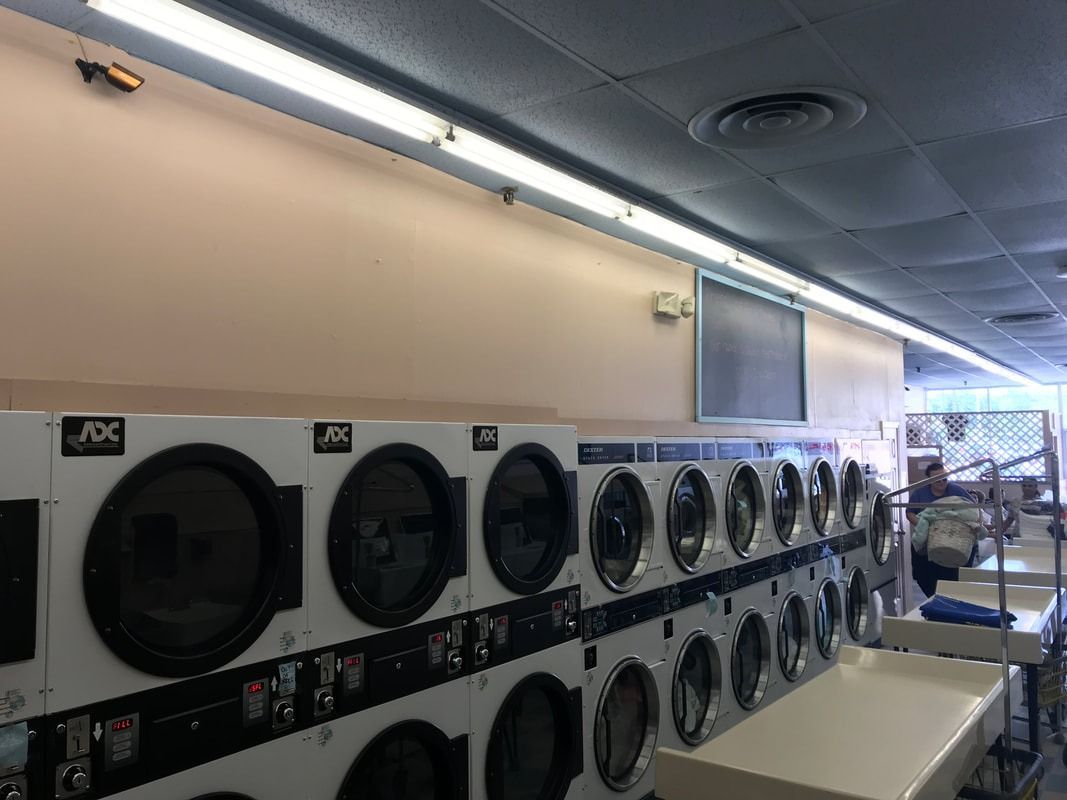 Row of laundry dryers in a laundromat, with bright overhead lighting and folding tables in front