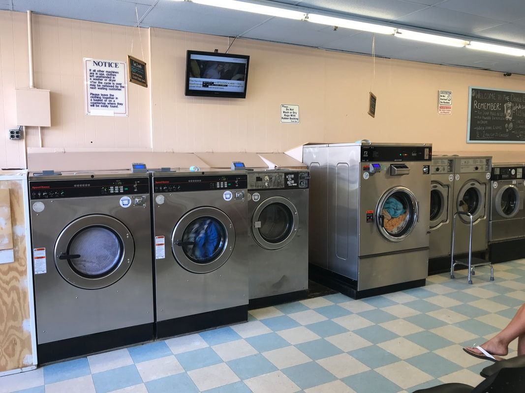 Laundry room with rows of front-load washers and dryers under a wall-mounted TV