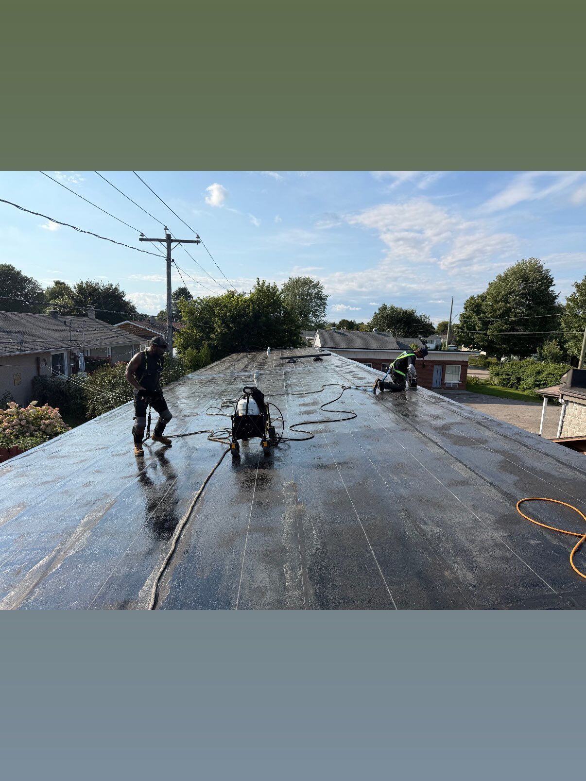 Des ouvriers nettoient un toit-terrasse mouillé à l’aide de tuyaux et de seaux, sous un ciel bleu, tandis que l’eau reflète la lumière