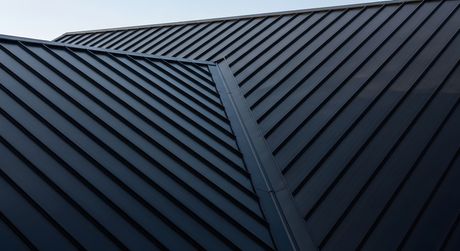 Panneaux de toiture en métal sombre avec des joints diagonaux et un faîtage central sur fond de ciel bleu