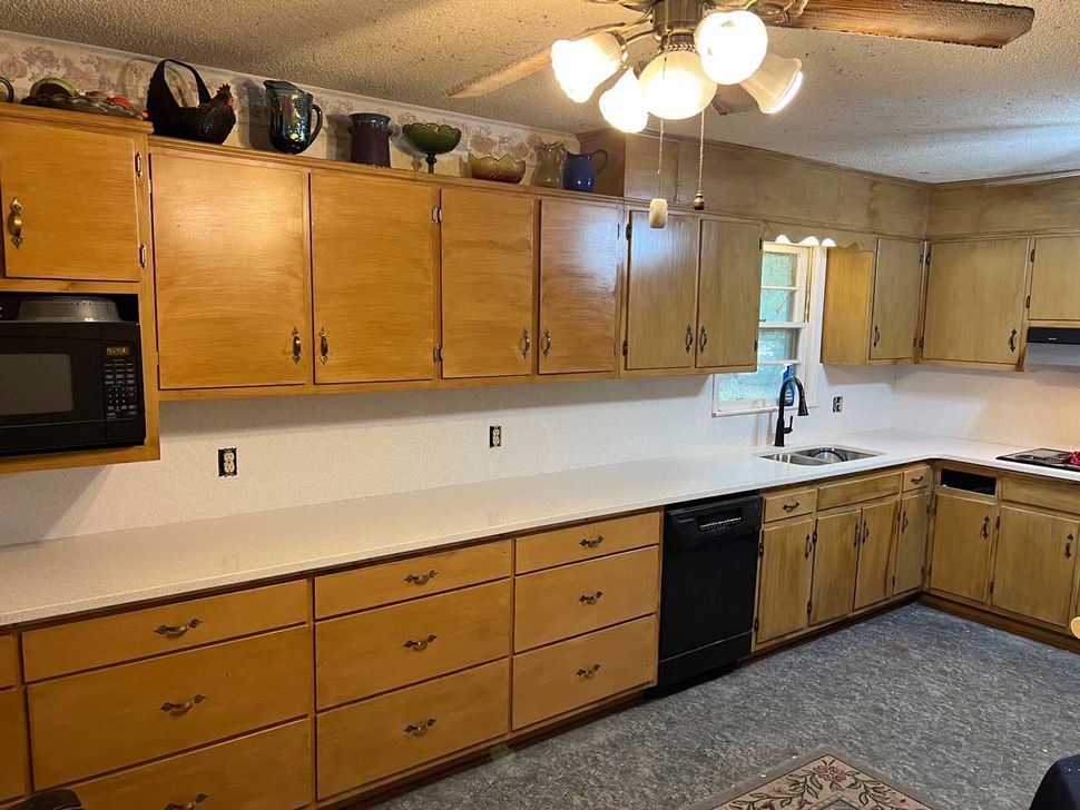 Long kitchen with wood cabinets, white countertops, black appliances, and a ceiling fan above.