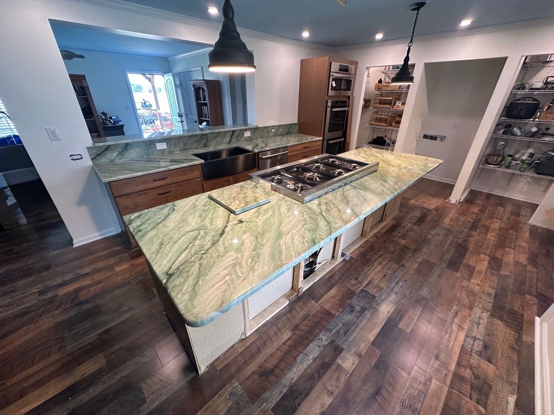 Modern kitchen with marble island, dark wood floors, pendant light, and open shelving.