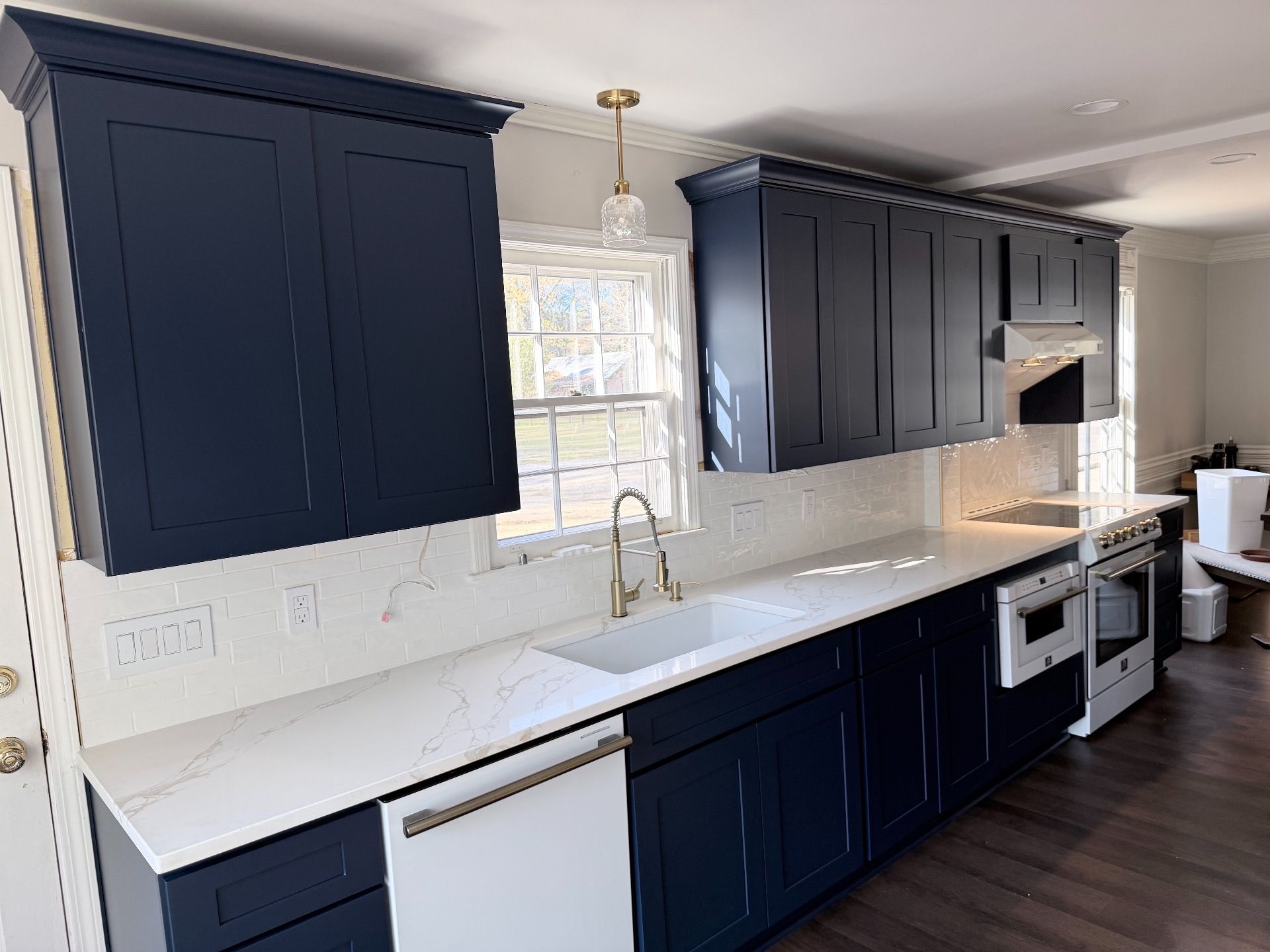 Modern kitchen with navy cabinets, white countertops, stainless appliances, and a window above the sink