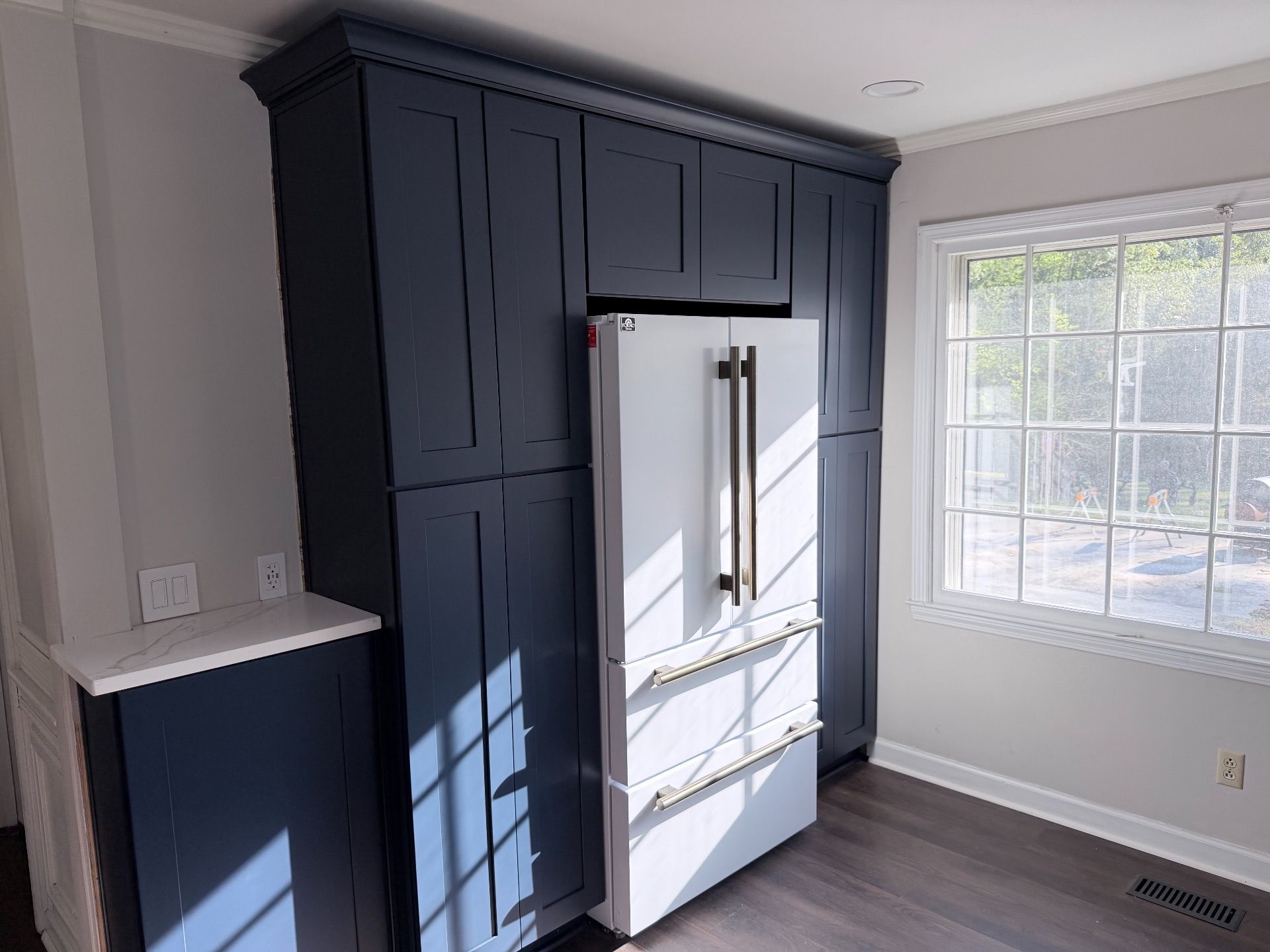 Kitchen with dark blue cabinets, white refrigerator, and bright window light.