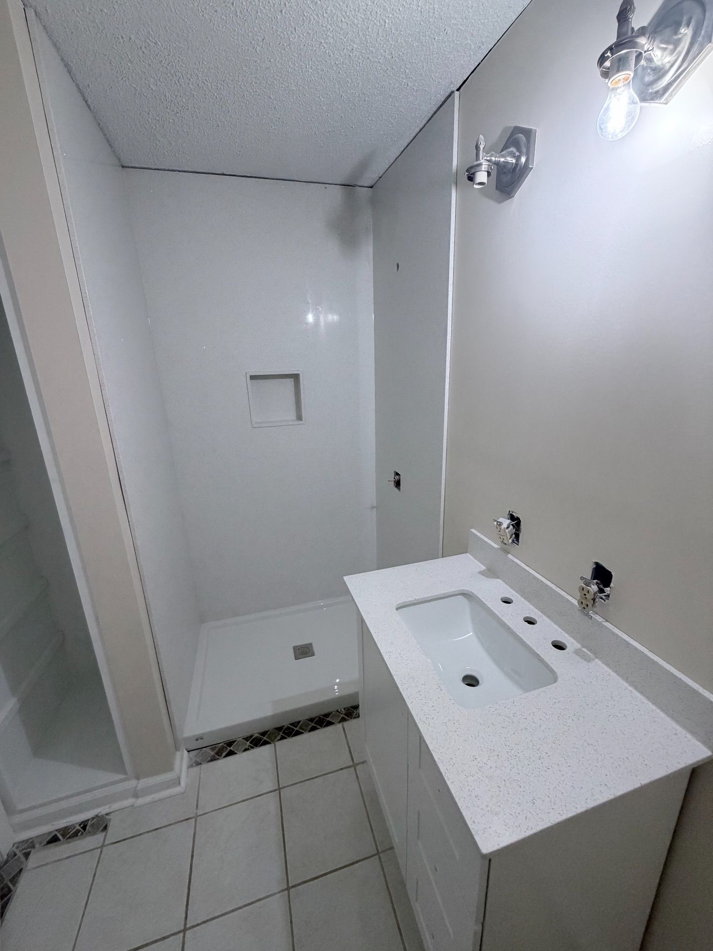 Small white bathroom with shower, sink, toilet, and tiled floor.
