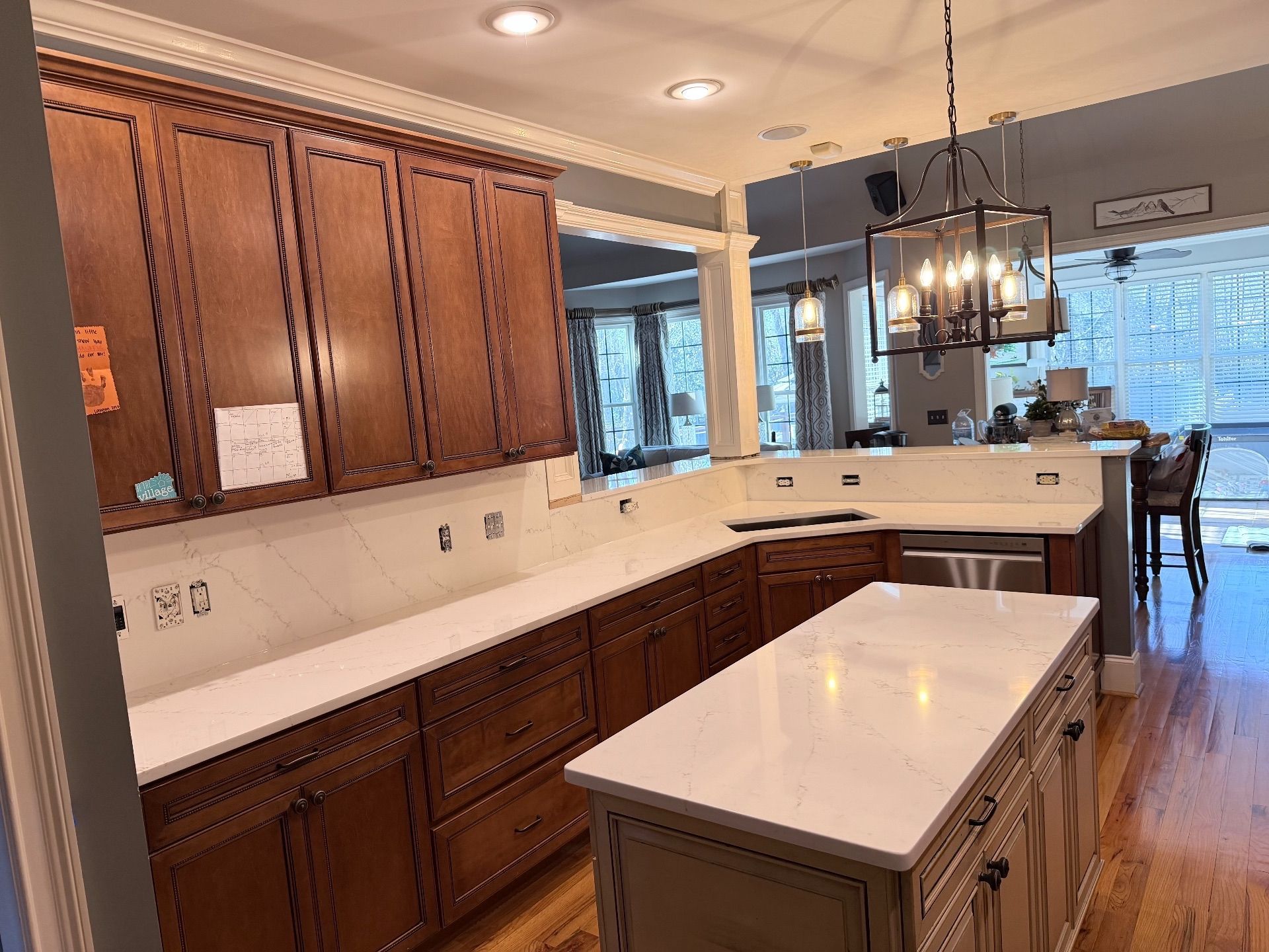 Bright kitchen with wood cabinets, white countertops, island, hardwood floors, and a dining area near windows.