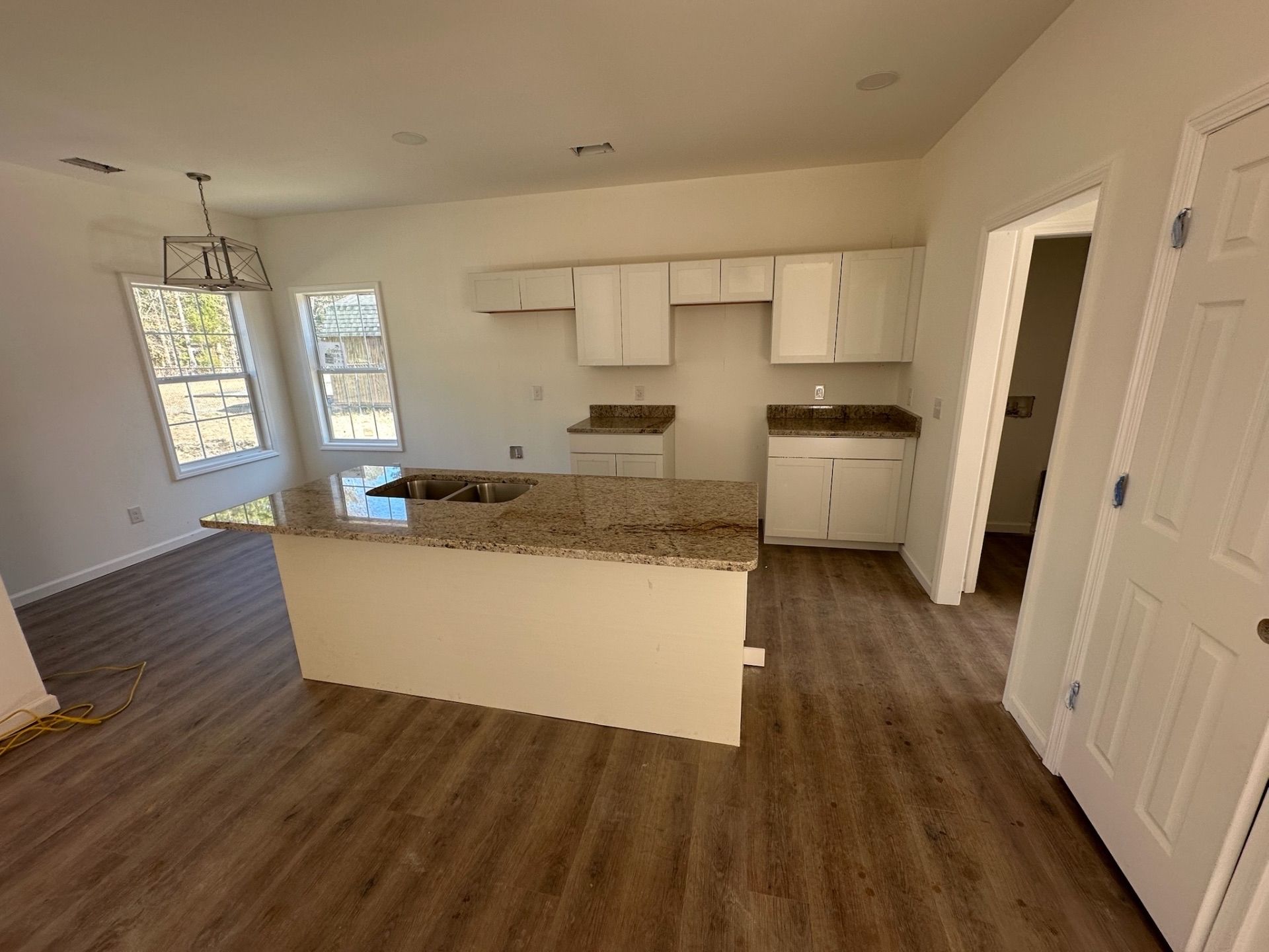 Empty modern kitchen with island, white cabinets, granite counters, and wood-look flooring.