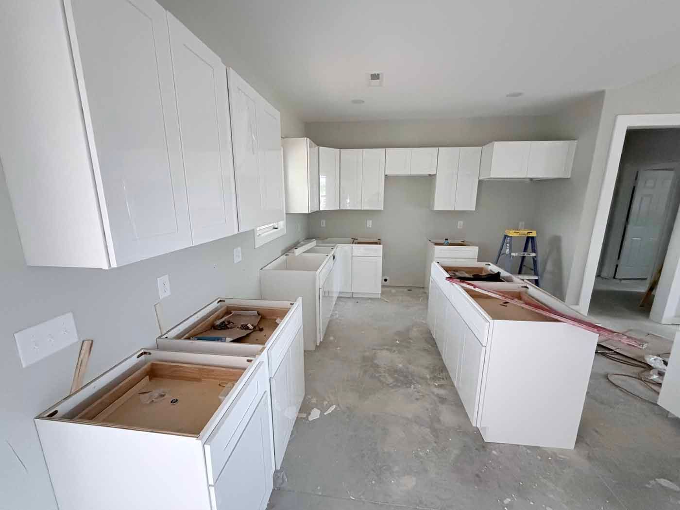 Unfinished white kitchen with cabinets and countertops installed, concrete floor, and no appliances.