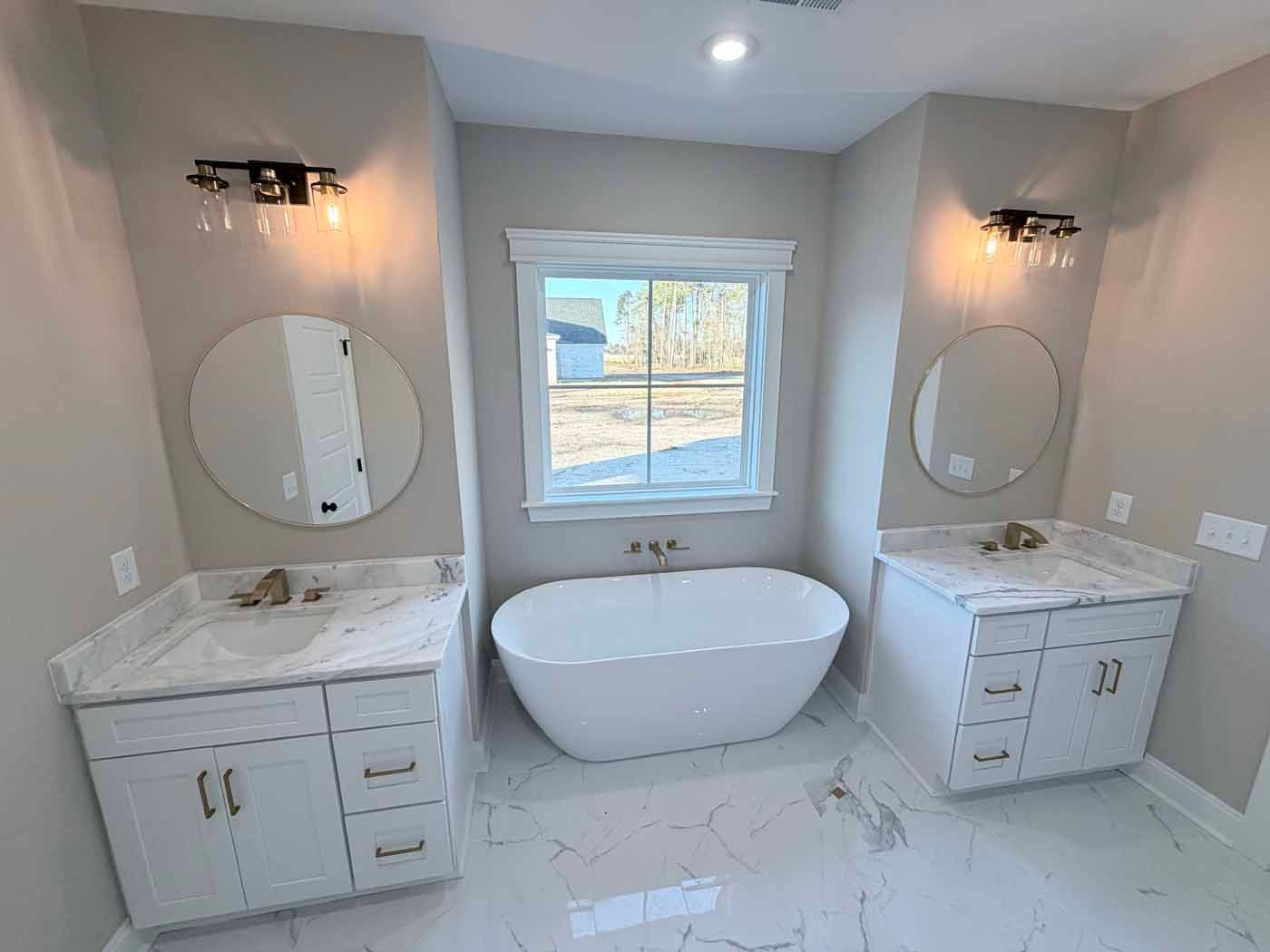Bright modern bathroom with freestanding tub, double vanity, round mirrors, and white marble tile layout