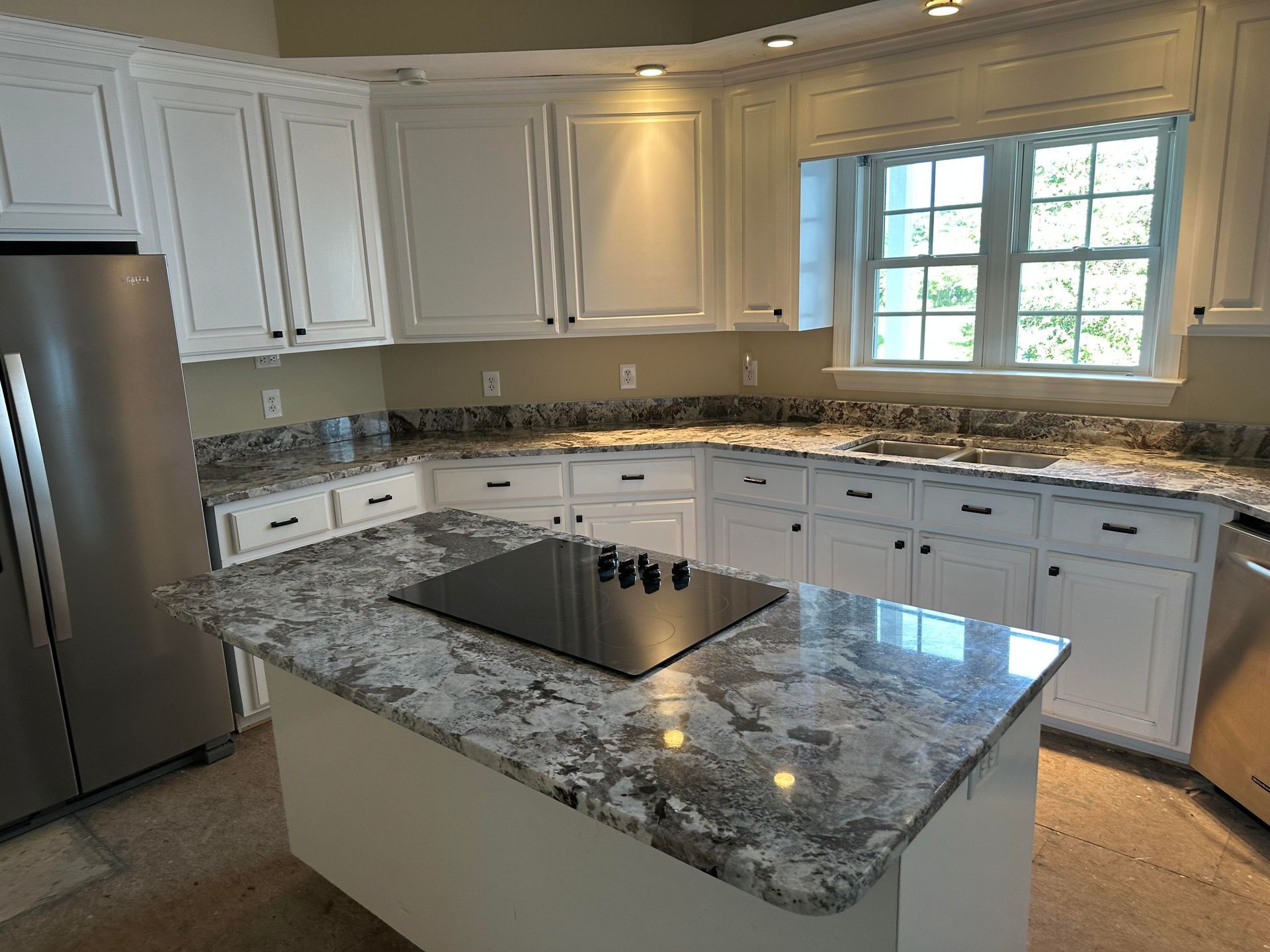 White kitchen with granite countertops, island with stovetop, stainless steel appliances.