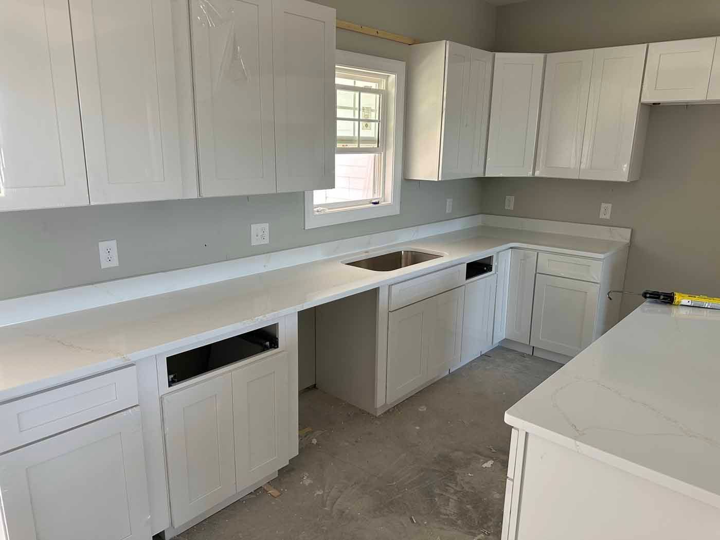 Empty white kitchen with unfinished cabinets, countertop, and a small window above the sink.