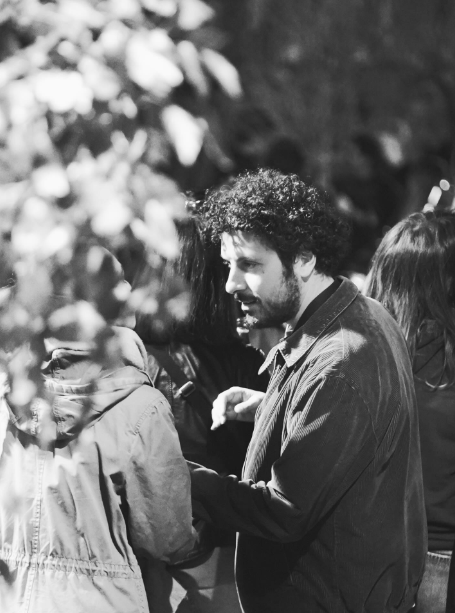 Due persone che parlano all'aperto, una delle quali tiene in mano una macchina fotografica tra la vegetazione sfocata.
