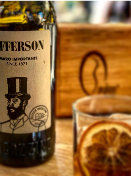Una bottiglia di whisky Lafferson accanto a un bicchiere di cocktail agli agrumi su un tavolo di legno.
