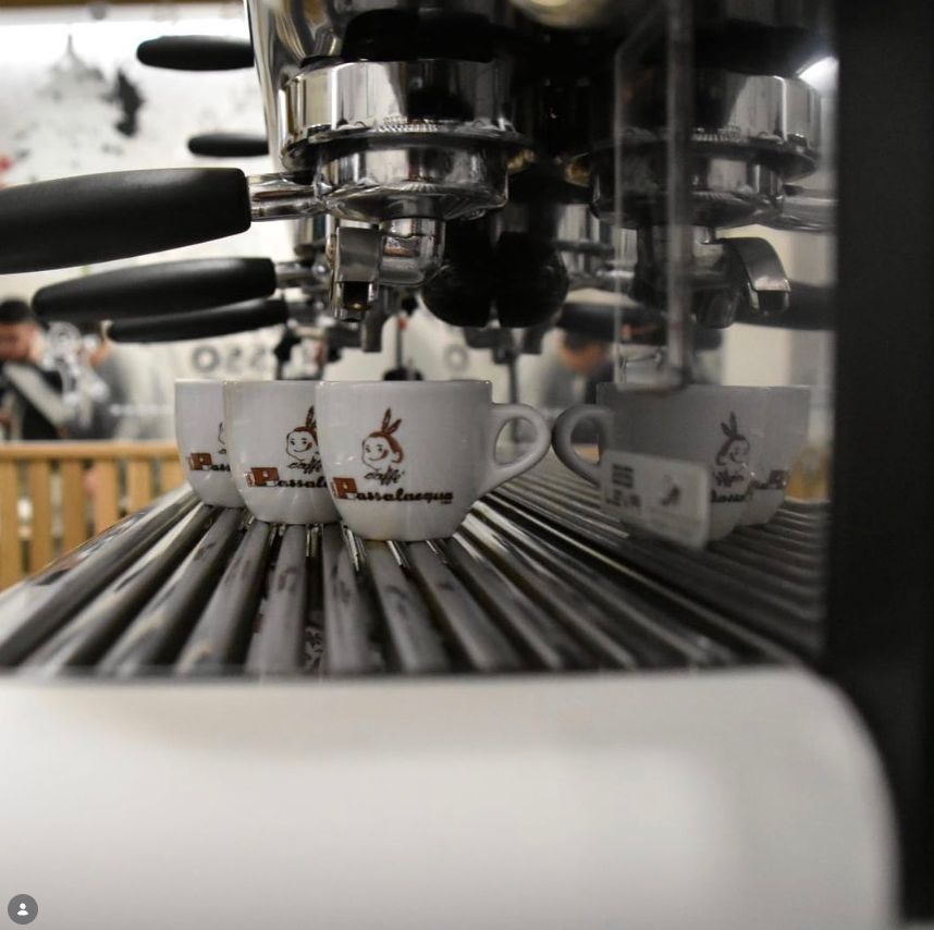 Macchina per caffè espresso che versa l'acqua in tazze bianche di marca posizionate su un vassoio raccogligocce in metallo.
