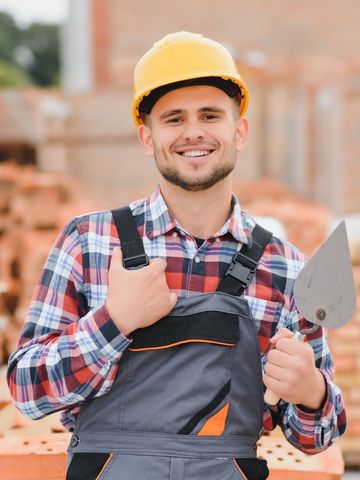 Un homme portant un casque et une salopette tient une truelle.
