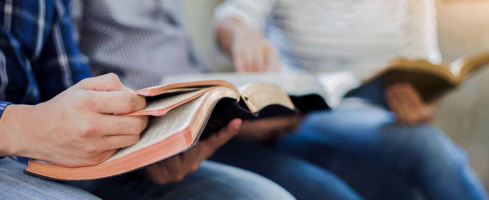 Close-up of a person holding an open Bible, with two more people in the background also holding Bibles.