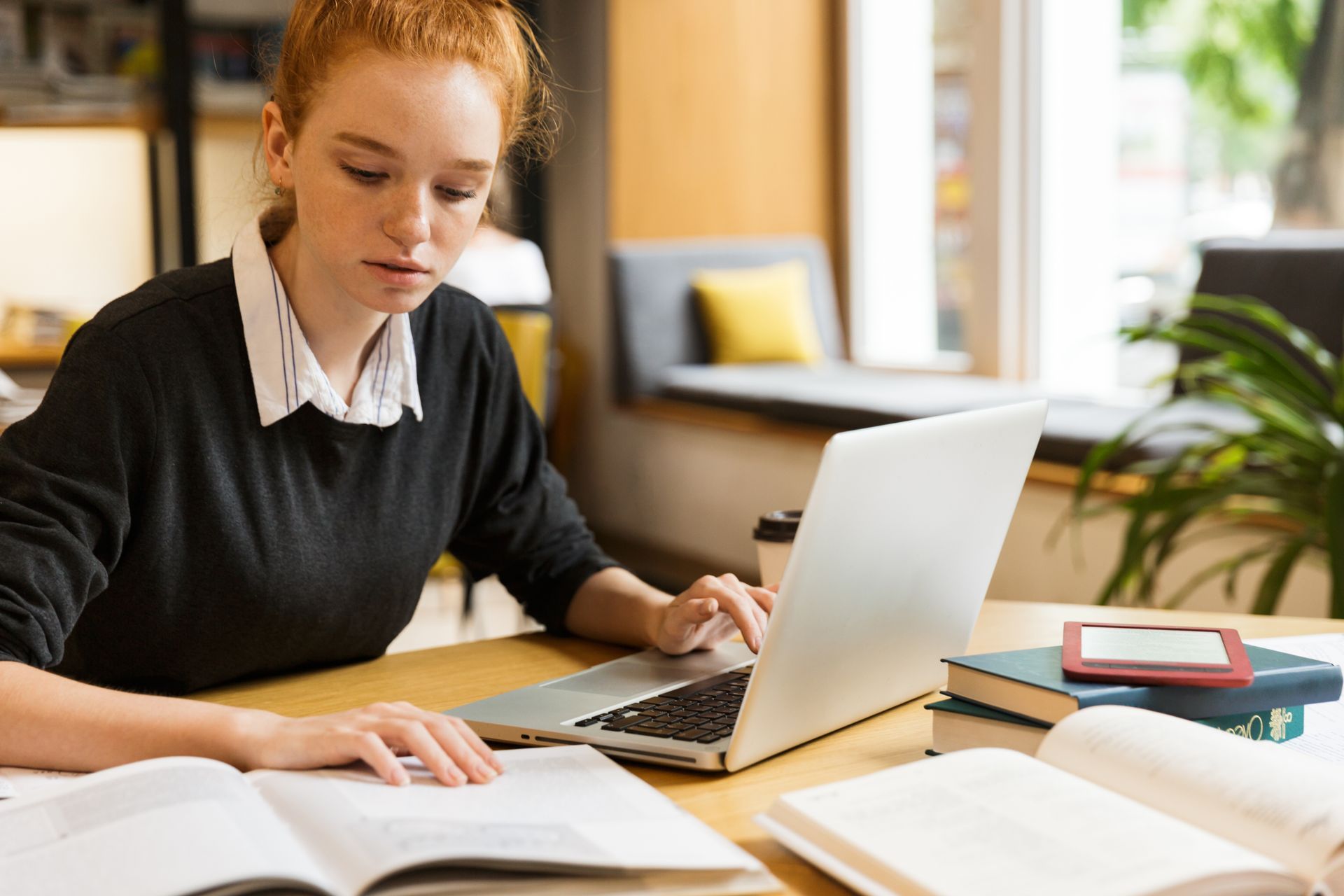 Image of a young woman sitting at a desk with a laptop and open book.