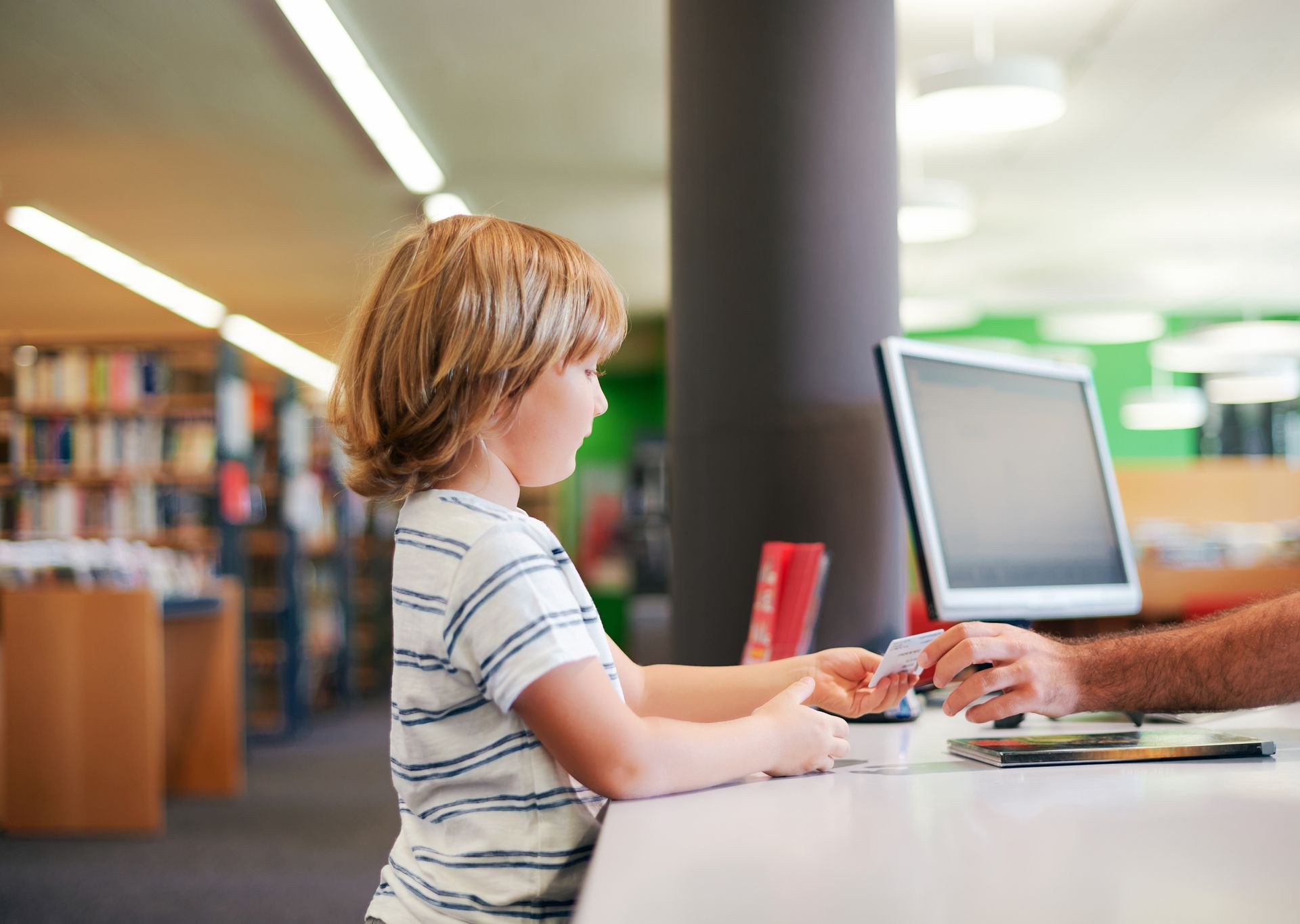 child handing a library card to an adult hand.