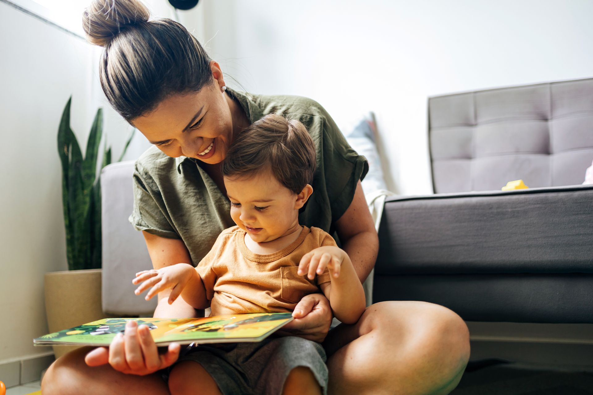 A woman sitting on the floor with a child on her lap and a picture book on the floor in front of them.