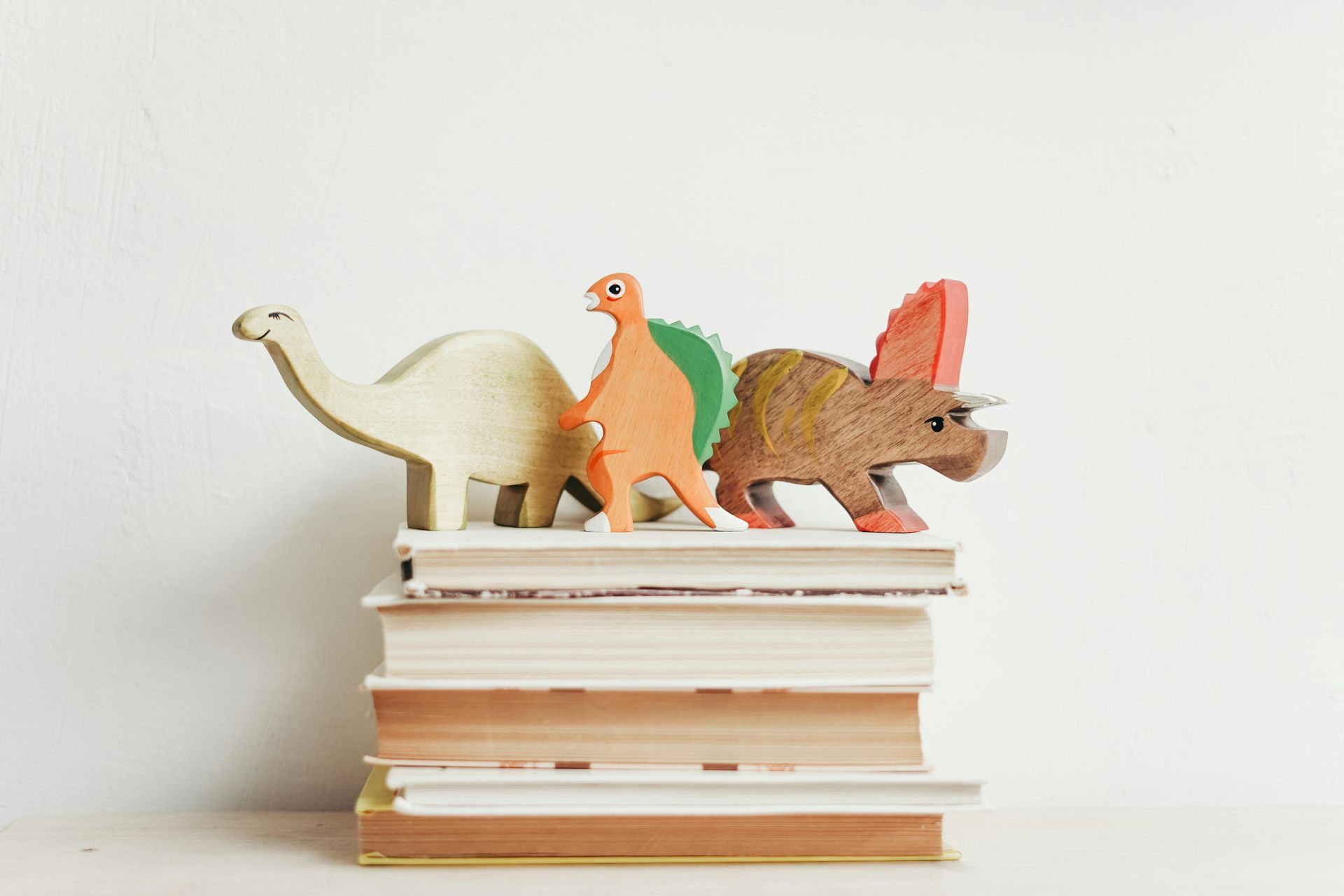 A group of three wooden dinosaur toys sitting on top of a stack of books.