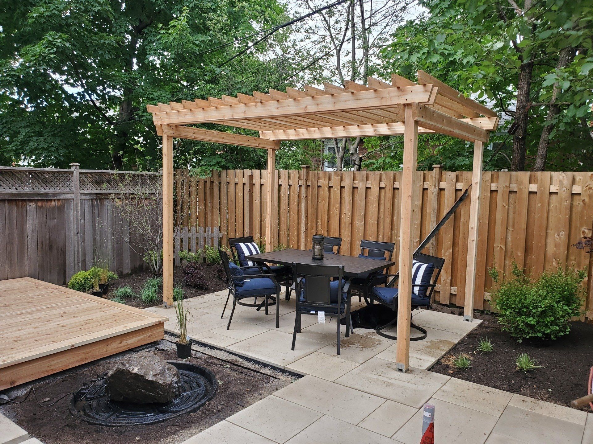 A wooden pergola with a table and chairs in a backyard.